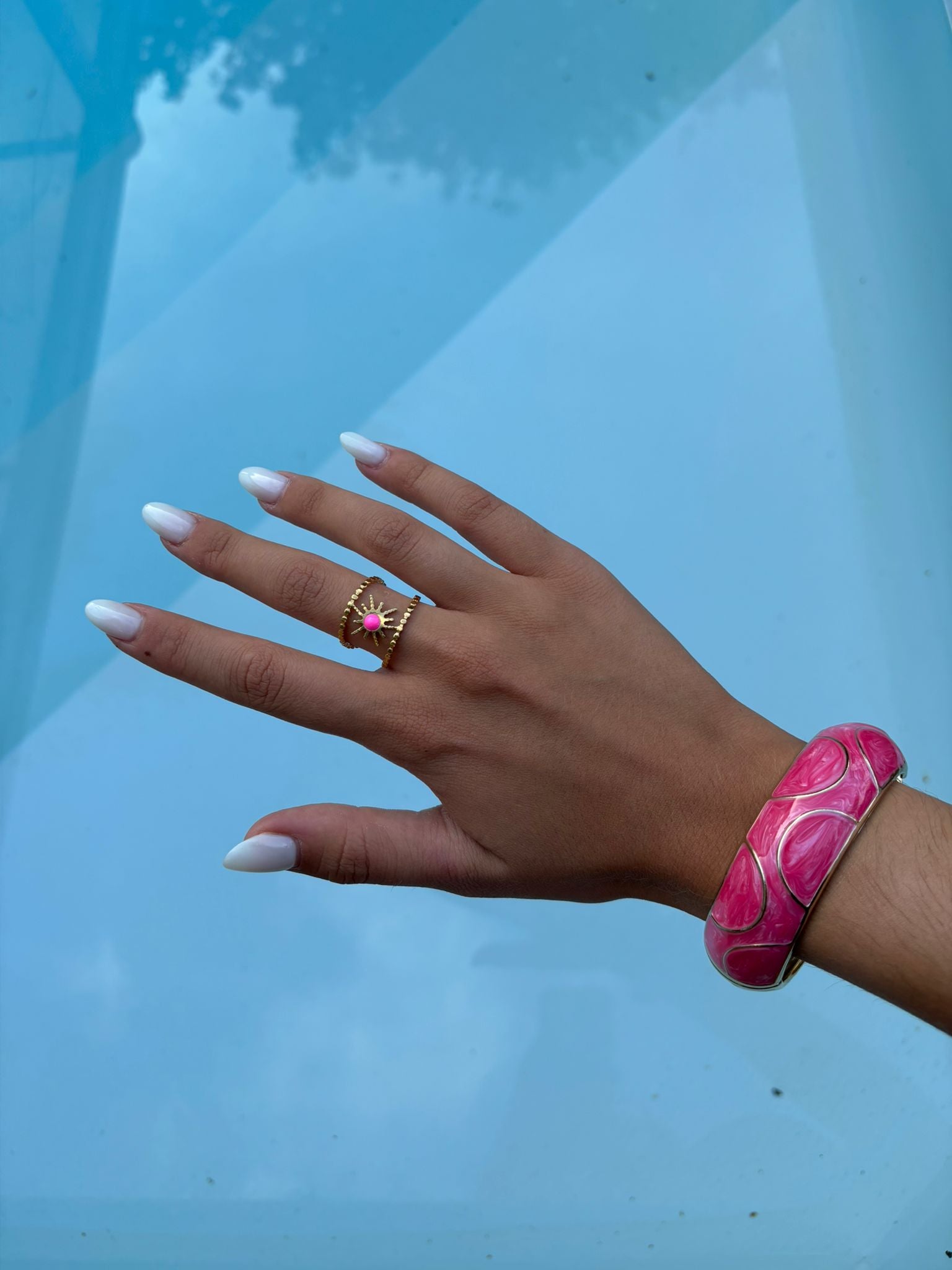 Bague dorée soleil rose portée au bord de la piscine