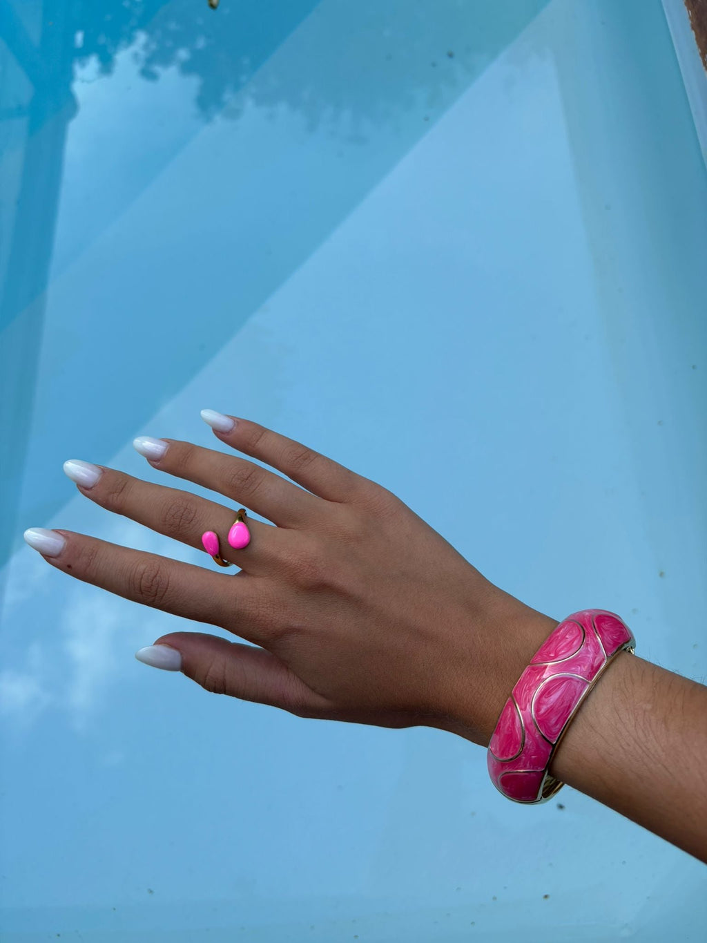 Bague dorée à deux gouttes roses portée au bord de la piscine