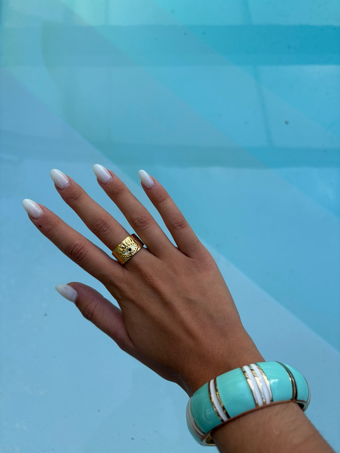 Bague chevalière dorée motif œil portée au bord de la piscine